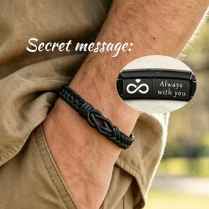 Puede incluir: Pulsera de cuero negro con un diseño tejido. La pulsera presenta un cierre negro con el texto "Always with you" y un símbolo de infinito. Las palabras "Secret message:" están escritas en cursiva blanca.