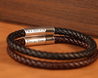 Puede incluir: Se muestran dos pulseras de cuero trenzado, una negra y otra marrón. Las pulseras tienen cierres plateados con texto grabado: "J & k 2025.4.18" y "I love you forever". Las pulseras están sobre una superficie marrón.