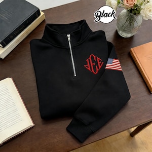 May include: Black quarter-zip sweatshirt with a red monogram and an American flag patch on the sleeve. The sweatshirt has a silver zipper and the word "Black" in a circular design.
