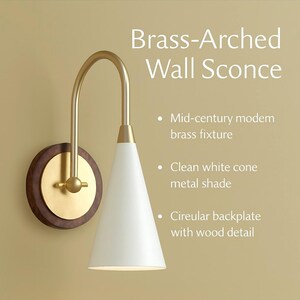 May include: A brass-arched wall sconce with a white cone shade and a circular backplate with wood detail. The fixture has a mid-century modern design.
