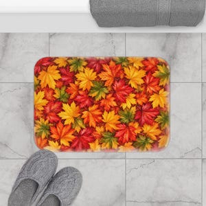 May include: A rectangular bath mat featuring a vibrant, dense pattern of autumn maple leaves in shades of bright red, golden yellow, burnt orange, and deep green. The design covers the entire surface of the mat with overlapping foliage.