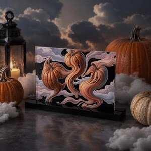 Könnte beinhalten: Ein rechteckiger Acrylblock mit einer surrealen Illustration von drei orangefarbenen Kürbissen, die sich vor einem schwarzen Hintergrund in wirbelnde, rauchartige Formen verwandeln. Das Kunstwerk ist auf einem soliden schwarzen Sockel montiert.