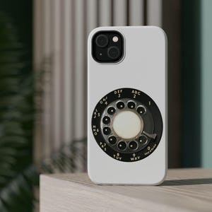May include: A white phone case with a black rotary dial design. The dial has white numbers and letters, including "DEF 3", "ABC 2", and "OPERATOR". The case has a modern smartphone camera array.