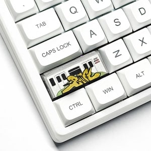 May include: A white keyboard with a custom keycap depicting a subway train with yellow graffiti. The keycap is positioned between the CTRL and WIN keys, replacing the original key.