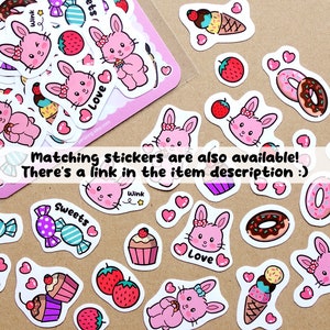 Op de afbeelding: Een vel met roze en witte stickers met schattige konijntjes, donuts, ijshoorns, cupcakes, snoepjes en hartjes. De stickers hebben zinnen zoals "Hallo!" en "Liefde" erop.