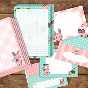 Op de afbeelding: Een set briefpapier met een roze en groene kleurstelling en een konijnenontwerp. De set bevat gestreept papier, enveloppen en kaarten met stippen. De tekst "HELLO!" staat op een van de kaarten.