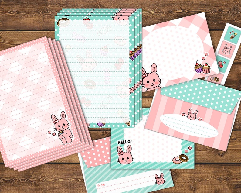 Op de afbeelding: Een set briefpapier met een roze en groene kleurstelling en een konijnenontwerp. De set bevat gestreept papier, enveloppen en kaarten met stippen. De tekst "HELLO!" staat op een van de kaarten.