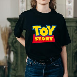 May include: Black t-shirt featuring the "Toy Story" logo in yellow, red, and blue. The shirt has a crew neck and short sleeves. The text "TOY STORY" is prominently displayed on the front.