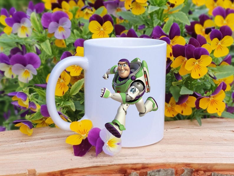 May include: White ceramic mug featuring a colorful graphic of Buzz Lightyear from Toy Story in a running pose. The mug is set against a backdrop of yellow and purple pansies, creating a cheerful and playful aesthetic.