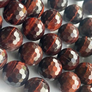 May include: Close-up of faceted, round beads in shades of deep red and brown. The beads have a geometric pattern of small, reflective facets. The beads are likely gemstones or decorative elements for jewelry making or crafts.