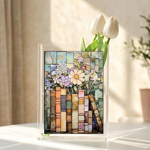 May include: A clear acrylic vase with a stained-glass panel featuring a floral arrangement and books. The flowers include daisies and other blooms in shades of white, pink, and purple. The books are in various colors, including orange, brown, and green.