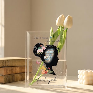 May include: A clear acrylic vase with a silhouette of a woman's head, filled with water and holding white tulips. The silhouette features a floral design and the text "Just a woman who loves books" and the name "Aaliyah".