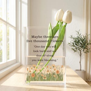May include: A clear rectangular vase with a floral design at the bottom, holding water and three white tulips. The vase has the text "Maybe there are five thousand Flowers" and a quote about blooming.