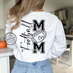 May include: White sweatshirt with a black graphic that says "Football Mom" with a football and heart design. The word "MOM" is in bold, block letters. The sweatshirt is a long-sleeved crew neck.