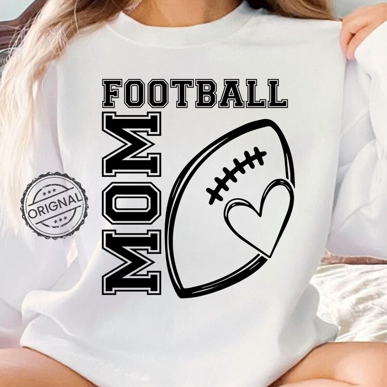 May include: White sweatshirt with the words "FOOTBALL MOM" in black block letters. A black and white football graphic with a heart is on the front. A circular "ORIGINAL" stamp is on the left.