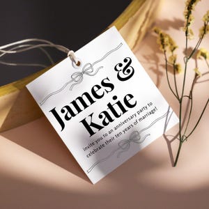 May include: A white invitation card with the names "James & Katie" in bold black font. The card is decorated with bow and ribbon designs and includes the text "invite you to an anniversary party to celebrate their ten years of marriage!"