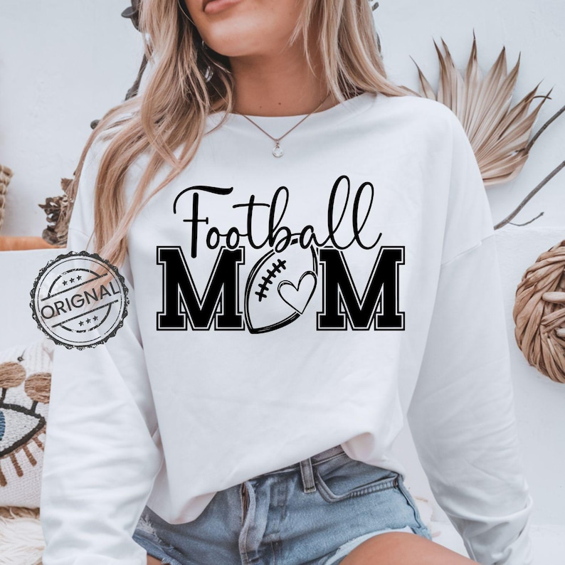 May include: White sweatshirt with the text "Football MOM" in black. The design includes a football and a heart. The word "ORIGINAL" is stamped on the left side of the sweatshirt.