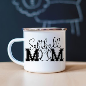 May include: White enamel mug with a silver rim and a black handle. The mug features the words "Softball MOM" in a script font and bold block letters, with a softball graphic in the center.