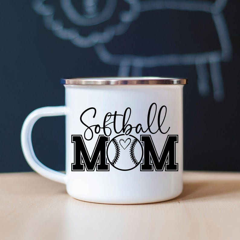 May include: White enamel mug with a silver rim and a black handle. The mug features the words "Softball MOM" in a script font and bold block letters, with a softball graphic in the center.