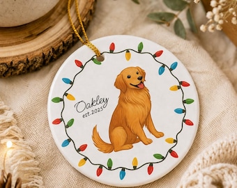 Könnte beinhalten: Runder, weißer Keramik-Weihnachtsschmuck mit einer Illustration eines Golden Retrievers. Der Schmuck ist von einer Girlande aus bunten Weihnachtslichtern umgeben. Der Name des Hundes, "Oakley", und das Jahr "est.2025" sind auf dem Schmuck geschrieben.