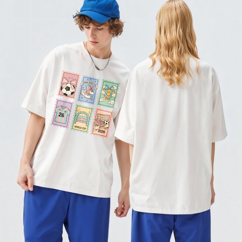 May include: White t-shirt with a colorful graphic of six postage stamp-style images, including a soccer ball, a shoe with a bow, and a soccer goal. The shirt is worn with blue shorts and a blue baseball cap.