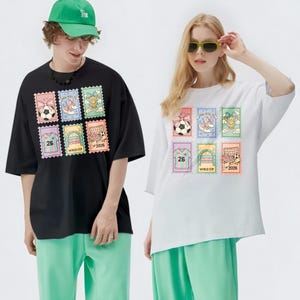 May include: Black and white t-shirts with a colorful stamp design featuring soccer balls, shoes, trophies, and soccer goals. The shirts have short sleeves and are paired with green pants. The stamps include the number "26" and the text "WORLD CUP 2026".