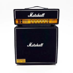May include: A black Marshall JCM 800 Lead Series amplifier with a matching cabinet. The amplifier has gold knobs and a black handle. The text "Marshall" is in white script on both the amplifier and cabinet.