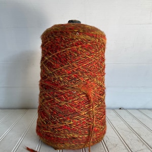 May include: A skein of yarn in a mix of red, orange, and brown colors. The yarn is wound around a cardboard tube.
