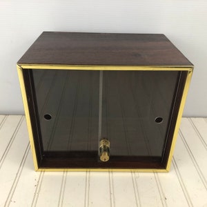 May include: A dark brown wooden display case with a glass front and a brass trim. The case has a lock and key.
