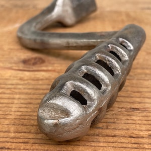 May include: A cast iron wrench with a curved handle and a textured grip. The wrench is silver in color and appears to be vintage. The tool is designed for tightening or loosening nuts and bolts.