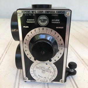 May include: Black Split Image Transit by Hopkins Mfg. Corp. Features a black body with silver accents, dials, and knobs. The text "HOPKINS MFG. CORP. EMPORIA, KANSAS" is visible. Includes the text "ABOVE TARGET" and "BELOW TARGET".