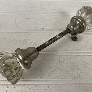 May include: A pair of antique glass door knobs with a silver finish and a threaded metal rod connecting them.