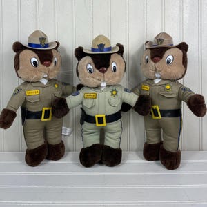 May include: Three plush chipmunk toys wearing khaki-colored sheriff uniforms and hats. Each toy has a brown face, ears, and feet, with a tan hat and a black belt. The uniforms have patches and the name "Chipper".