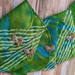 Puede incluir: Cuatro bolsos de mano de tela estampada verde y azul con adornos florales y de cuentas. Los bolsos tienen un cierre de solapa plegada y están dispuestos sobre una superficie de madera. La tela tiene un diseño de rayas.