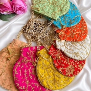 May include: A collection of colorful, embroidered drawstring pouches in shades of green, blue, orange, white, red, yellow, pink, and peach. Each pouch features gold floral embroidery and a beaded drawstring. Pink roses are in the background.