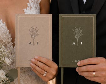 May include: Two hardcover books with fabric covers, one in beige and one in olive green. Each book features a gold-stamped floral illustration, the initials A and J, and the date 09.20.24. Both books include a matching ribbon bookmark.