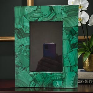 May include: A rectangular picture frame with a malachite design. The frame is a vibrant green with a mosaic pattern. The frame is displayed on a dark surface, with a dark background.