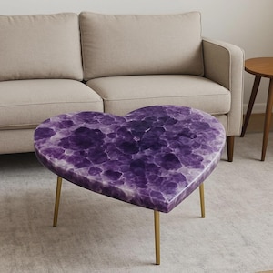 May include: A heart-shaped coffee table with a purple amethyst top and gold-colored legs. The table is approximately 30 inches wide and 28 inches deep, with a height of 16 inches. The table is in front of a beige sofa.