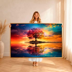 May include: A rectangular wall art print in a thin gold frame featuring a vibrant sunset landscape with a central tree displaying pink and orange foliage. The scene includes a reflection of the tree and the colorful sky on a calm water surface.
