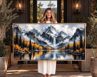 Può includere: Un dipinto di paesaggio rettangolare in una sottile cornice dorata che raffigura una catena montuosa innevata con una cascata centrale, un lago calmo e una fitta foresta di alberi sempreverdi e giallo oro riflessi nell'acqua.