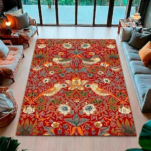 Puede incluir: Una alfombra rectangular roja con un detallado diseño floral y de pájaros. La alfombra presenta un diseño simétrico con pájaros, flores y follaje en tonos dorados, verdes y grises. La alfombra está colocada sobre un suelo de madera clara.