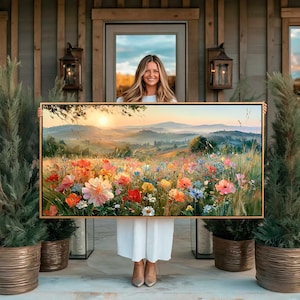 May include: A rectangular landscape wall art print featuring a vibrant meadow of wildflowers in shades of pink, orange, yellow, and blue under a soft sunrise sky with rolling hills in the background, framed in a thin light-toned wooden border.