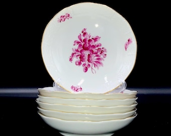 May include: A stack of white porcelain bowls with a scalloped edge and gold trim. Each bowl features a central magenta floral design and smaller floral accents. The bowls are stacked on a black background.