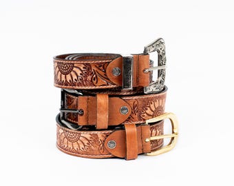 May include: Three stacked brown leather belts with sunflower designs and various buckle styles. The top belt has a decorative silver buckle, the middle one has a black buckle, and the bottom one has a gold buckle. The belts are on a white background.