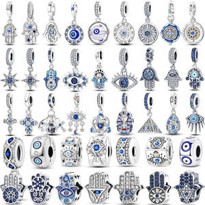 May include: A collection of silver-toned charm pendants with blue and clear crystal accents. Designs include the Hamsa hand, evil eye, stars, crosses, and other decorative shapes. These charms are designed for bracelets.