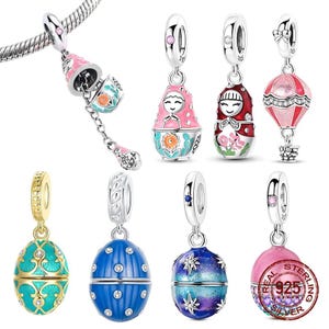 May include: A selection of silver charm pendants with vibrant enamel designs. The charms feature Matryoshka dolls, hot air balloons, and Fabergé egg styles. The charms are in pink, blue, red, and gold, with detailed patterns and sparkling embellishments.