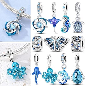May include: A collection of silver-toned jewellery charms featuring various marine life and celestial motifs. The charms are decorated with blue enamel, clear crystals, and heart-shaped stones, including designs of dolphins, a stingray, a seahorse, a turtle, an octopus, a lizard, a butterfly, and a teardrop-shaped pendant.