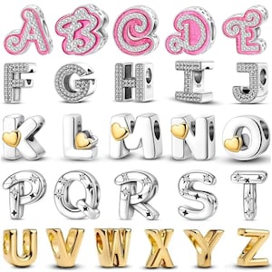 Könnte beinhalten: Eine Sammlung von Buchstabenanhängern in Silber- und Goldtönen. Einige Buchstaben haben rosa Emaille und klare Kristalle, andere goldene Herzakzente. Die Charms sind für Armbänder oder Halsketten konzipiert.