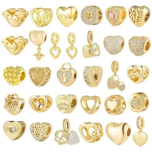 May include: A collection of gold-colored heart-shaped charms and pendants. Designs include openwork hearts, hearts with the word "Mom", and heart-shaped charms with embedded crystals. Some charms have a dangling design.