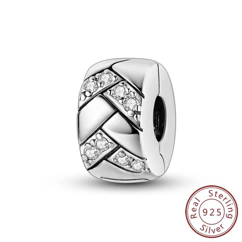 May include: A silver charm with a woven design, accented with clear, sparkling stones. The charm is a rectangular shape with a clasp on one side. The charm is made of 925 sterling silver.
